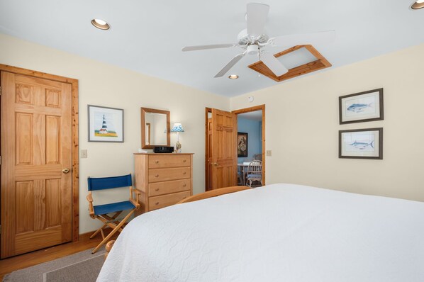 A bedroom with a bed, wooden wardrobe, dresser, and a ceiling fan.