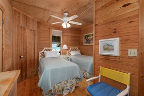 A wooden cabin room with two beds, a ceiling fan, a chair, and a framed picture on the wall.