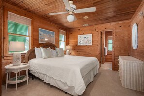 A wooden cabin bedroom with a bed, a ceiling fan, and a door leading to another room.