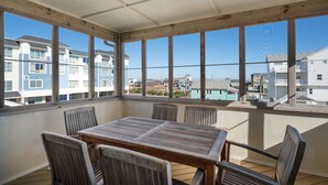 Un balcone coperto con tavolo e sedie in legno, ampie finestre che offrono vista sugli edifici e sulla spiaggia.