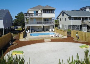 A two-story house with a backyard featuring a swimming pool, a patio with chairs, and a fenced area.