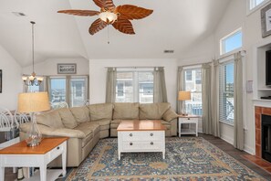 A living room with a sectional sofa, a wooden coffee table, a patterned rug, and a ceiling fan.