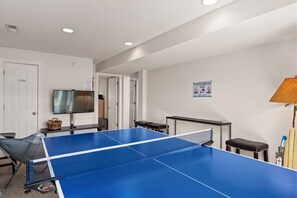 A room with a ping pong table, a television, and a beach house sign. - Mama Burts: Oceanside, community pool, hot tub, game room, elevator & short walk to the beach! (Nags Head)