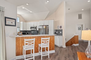 A modern kitchen with white cabinetry, a stainless steel refrigerator, and a wooden island with two white chairs.