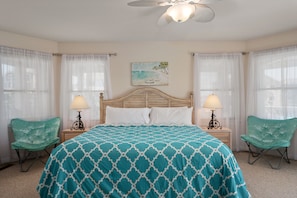 A bedroom with a large bed, two nightstands, two lamps, two chairs, and a ceiling fan.