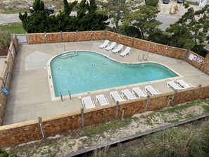 Una piscina con borde de ladrillo, rodeada de sillas de descanso y una terraza pavimentada.