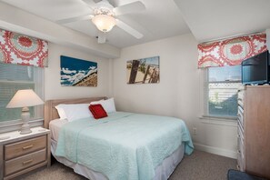 A bedroom with a bed, a nightstand, a lamp, a ceiling fan, and artwork on the walls.