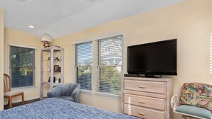 A bedroom with a bed, a television, a chair, a dresser, and a window with blinds.