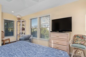 A bedroom with a bed, a television, a chair, a dresser, and a window with blinds.