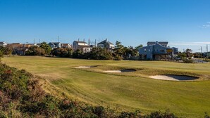 A golf course with sand bunkers, a clear sky, and residential houses in the background.