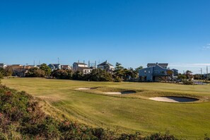 A golf course with sand bunkers, a clear sky, and residential houses in the background.