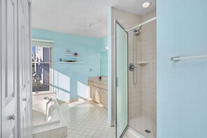 A bathroom with a glass shower, a bathtub, and a window.