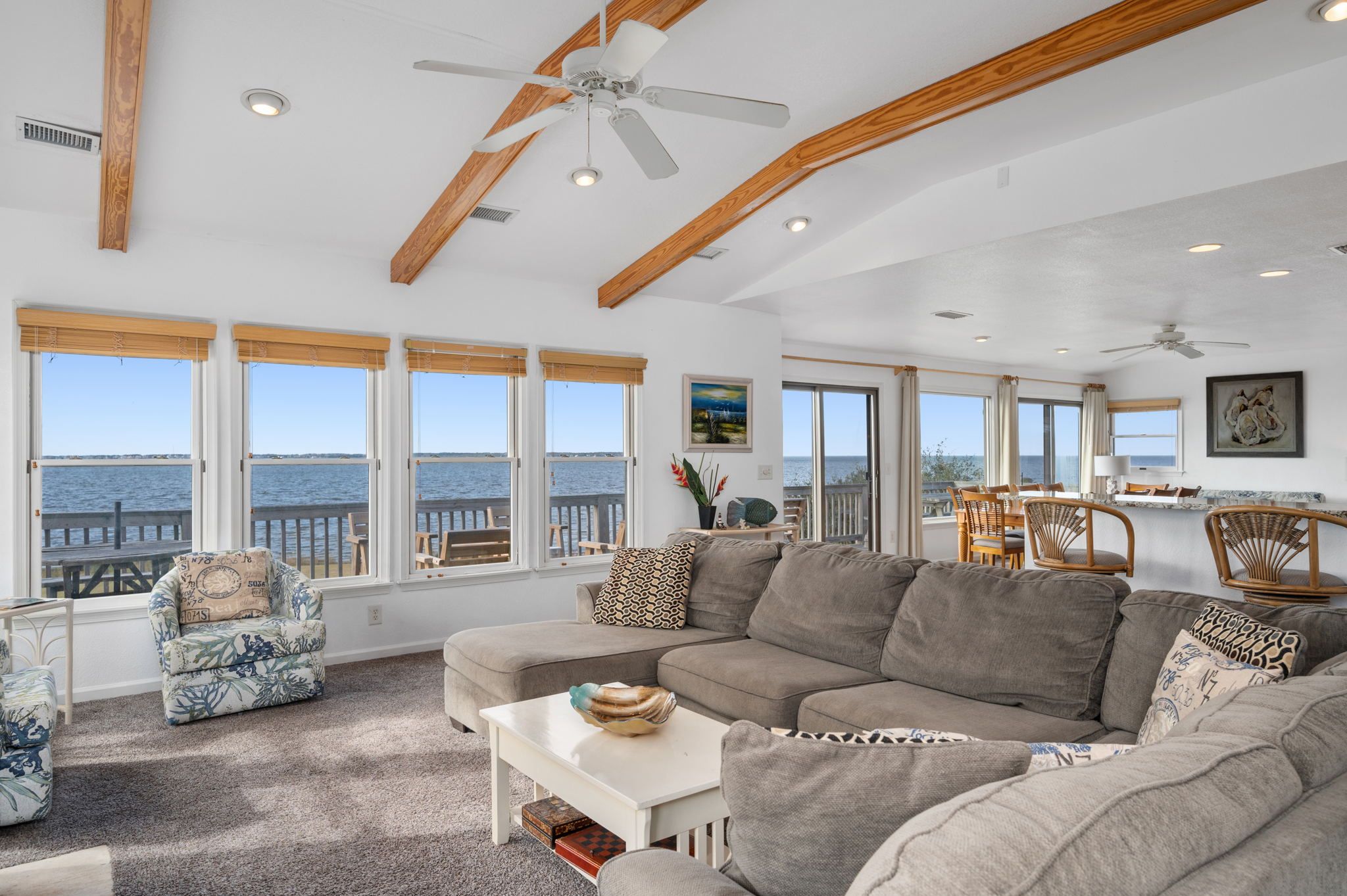 A spacious living room with a large gray sectional sofa, a white coffee table, and a dining area with wicker chairs.
