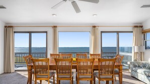 A dining area with a table and chairs, large windows with a view of the sea, and a ceiling fan.