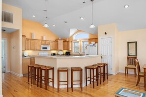 A kitchen with wooden cabinets, a central island with stools, and a dining area with chairs.