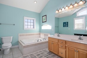 A bathroom with a bathtub, a toilet, a vanity with a sink, and a large mirror.