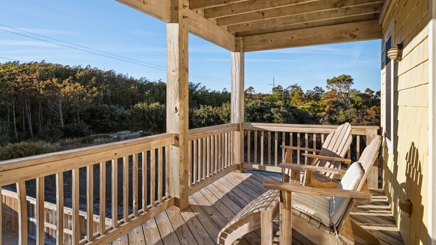 Una terraza de madera con barandilla, dos sillas Adirondack y vistas a un área boscosa.