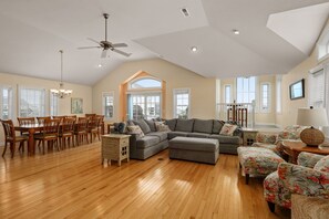A spacious living room with a dining area, wooden flooring, and large windows.