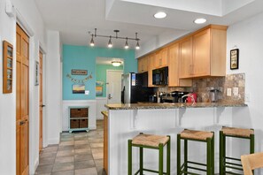 A modern kitchen with wooden cabinets, a central island with bar stools, and a teal accent wall.