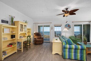 A living room with a sofa, armchairs, a bookshelf, and a ceiling fan.