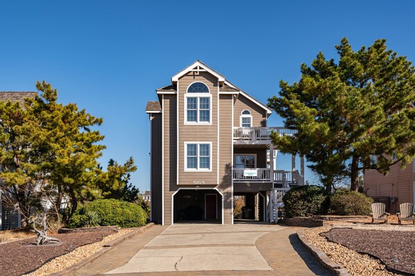 A two-story building with a central entrance, a balcony on the second floor, and a sign indicating it is part of a resort. - Wedges 13: Soundside, 13th fairway view, great community pool and tennis courts. ⛳☀️ (Nags Head)