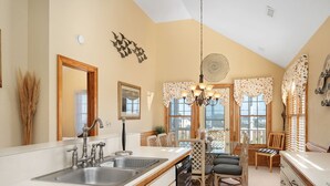 A kitchen with a double sink, wooden chairs, a dining table, and a chandelier. - Wedges 13: Soundside, 13th fairway view, great community pool and tennis courts. ⛳☀️ (Nags Head)