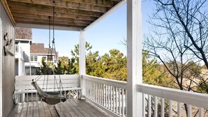 A wooden porch with a swing, white railings, and a view of a residential area with trees and houses. - Wedges 13: Soundside, 13th fairway view, great community pool and tennis courts. ⛳☀️ (Nags Head)