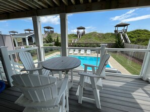 A covered outdoor area with a pool, white Adirondack chairs, and a table. - Sunset Beach House: Great views, private pool, hot tub, pool table & elevator (Nags Head)