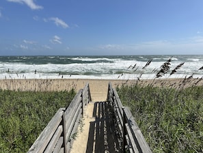 A wooden boardwalk leading to a beach with waves in the background.