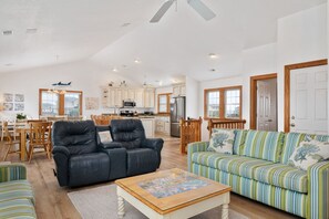Un vaste espace de vie comprenant un canapé en cuir noir, un divan à rayures et une table basse en bois.