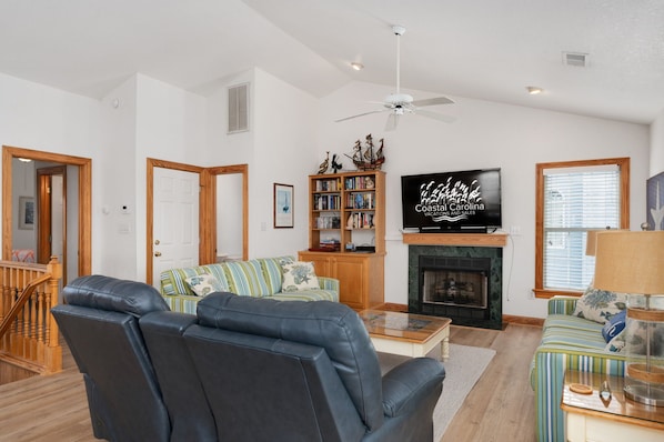 A living room with a fireplace, a television, a bookshelf, and a staircase.