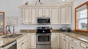 Cozinha com armários brancos, forno de aço inoxidável, micro-ondas e torradeira.