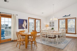A dining area with a wooden table and chairs, large windows with blinds, and a view of the outside. - Sunshine In My Pocket: Oceanside, private pool, hot tub, ping pong table, short walk to beach! (Nags Head)