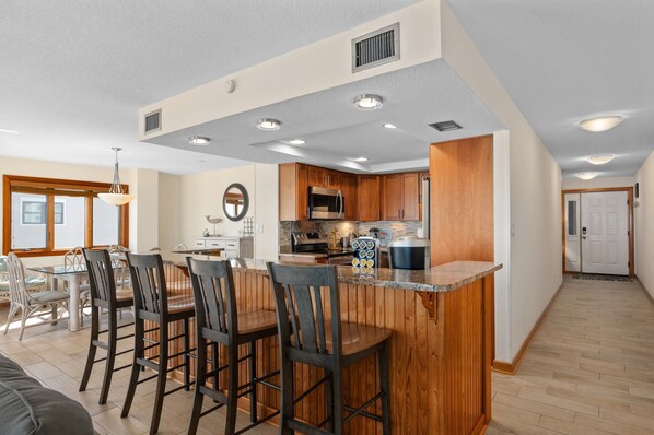 A modern kitchen with wooden cabinets, a central island with bar stools, and a dining area with a table and chairs.