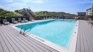 Una piscina rectangular con cubierta de madera, rodeada de sillas de descanso y una escalera que lleva a un nivel superior.