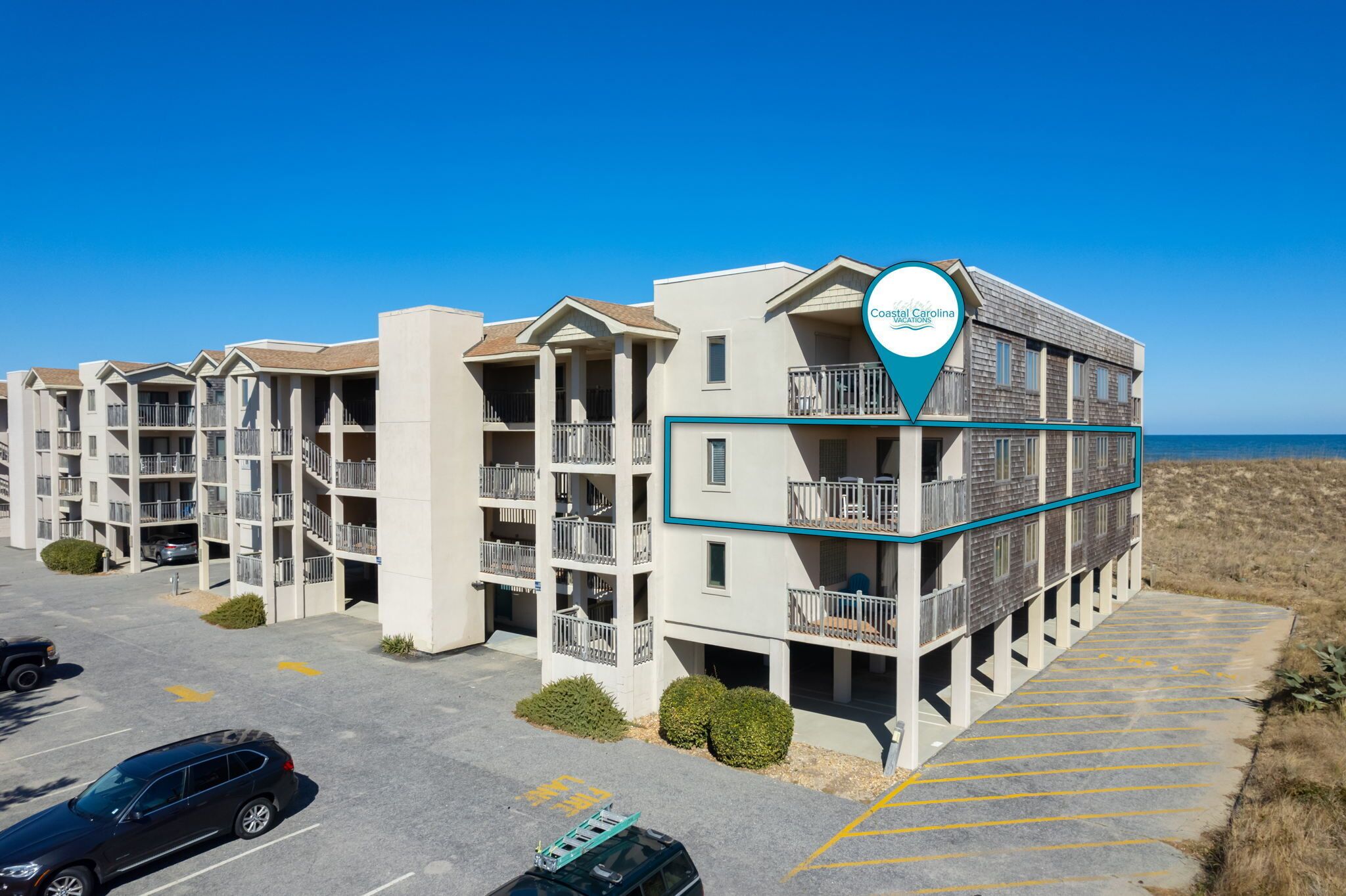 A multi-story hotel with balconies, a parking lot, and a view of the ocean.
