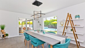 Een moderne eetruimte met een lange tafel, teal stoelen en een witte plafondlamp.