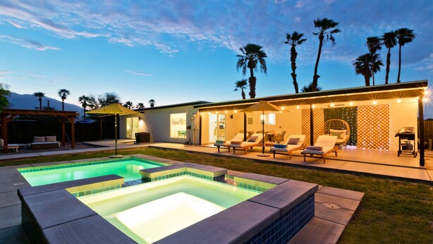 Een modern huis met een zwembad, terras en palmbomen.