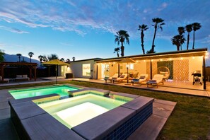 Ein modernes Haus mit Swimmingpool, Sitzgelegenheit im Freien und Palmen.