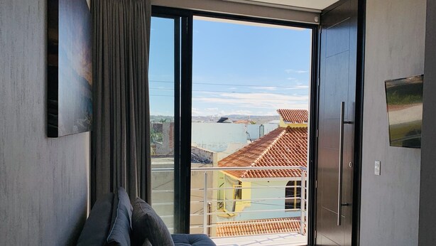 Uma sala de estar moderna com um sofá, uma janela grande e vista para edifícios e um corpo d'água.