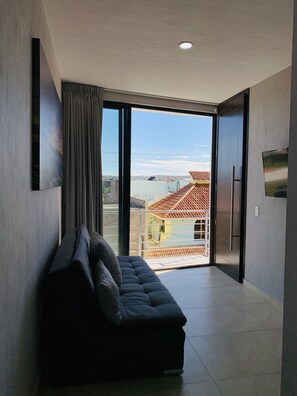 A modern living room with a sofa, a large window, and a view of buildings and a body of water. - Comfortable Modern Stay by Hidden Gem Vacation Homes (Zapotlanejo)