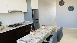 Cozinha moderna com bancada de mármore, eletrodomésticos de aço inoxidável e um espaço de refeições com cadeira e mesa.