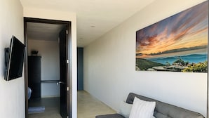 Uma sala de estar moderna com um sofá cinzento, uma TV de tela plana na parede e um quadro paisagístico grande retratando um pôr do sol.