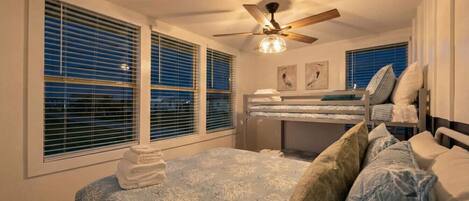 Un dormitorio con cama, ventilador de techo y ventana con persianas.