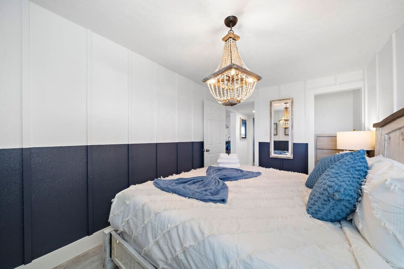 A bedroom with a large bed, a chandelier, and a mirror on the wall.