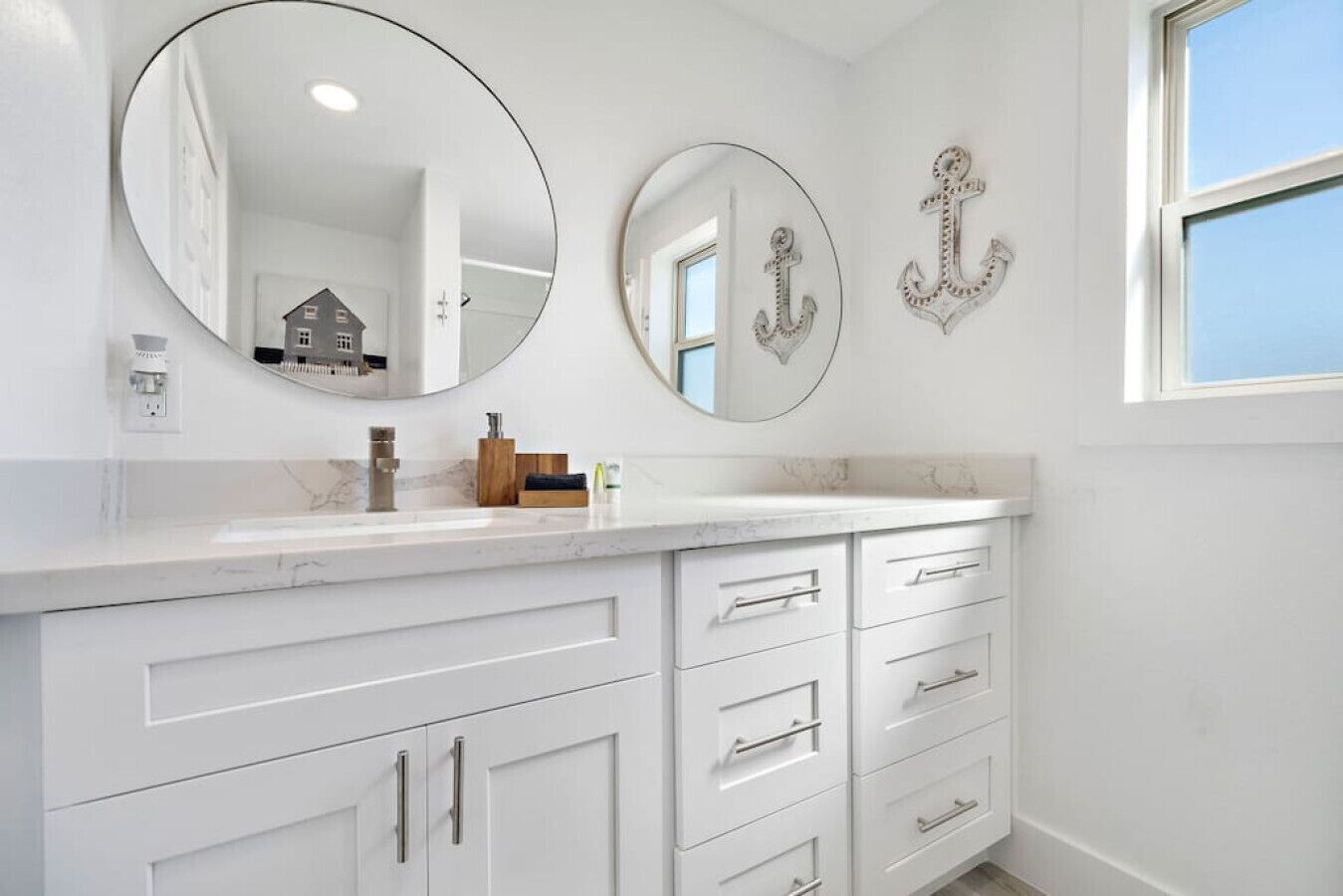 Une salle de bain avec un meuble-lavabo blanc, deux miroirs ronds et des éléments décoratifs en forme d’ancre fixés au mur.