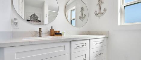 Une salle de bain avec un meuble-lavabo blanc, deux miroirs ronds et des éléments décoratifs en forme d’ancre fixés au mur.