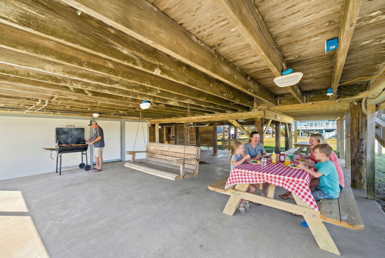 Un espacio al aire libre techado con una mesa de picnic, una parrilla y un columpio.