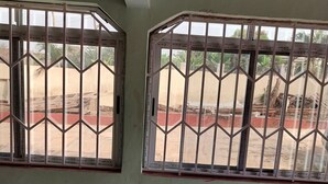 Una habitació amb dues finestres grans amb reixes metàl·liques, un terra de viqueta i una esquerda visible a la paret.