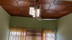 Una habitació amb sostre de fusta, un penjador de cristall i tres cadires, amb un finestral amb cortines.